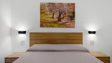 A bedroom with a wooden headboard, a bed with a quilted mattress, two bedside tables, and a wall-mounted painting.