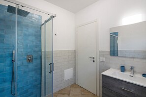 Un baño con cabina de ducha de vidrio, una puerta blanca, un lavabo con espejo y una toalla azul sobre la encimera.