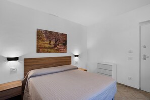 Un dormitorio con cama, mesitas de noche, un cuadro en la pared y una puerta.