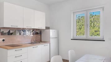 Une cuisine moderne avec des meubles blancs, un four encastré et une fenêtre donnant sur un paysage verdoyant.