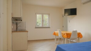 Une cuisine compacte dotée d’un four encastré, d’une fenêtre donnant sur un espace verdoyant et d’un coin repas avec une table et des chaises.