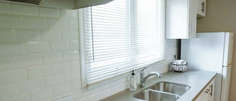 Una cocina con armarios blancos, estufa a gas, fregadero y refrigerador.