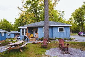 A blue cabin with a porch, outdoor seating, and a picnic table. - Sandpiper Cottage - 3-Bedroom Cottage – Family Friendly (Trent Lakes)