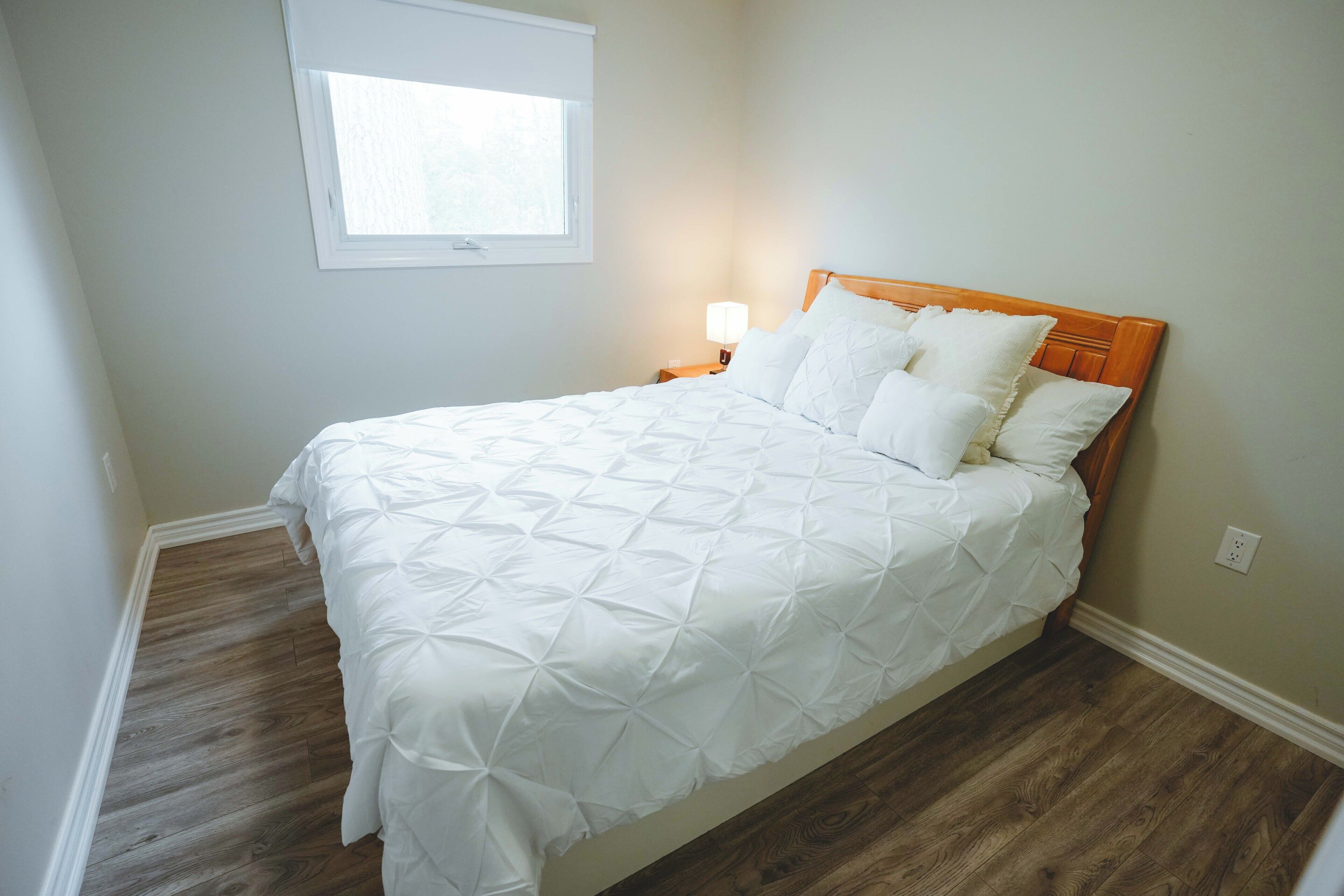 Un lit simple avec une tête de lit en bois, dans une pièce aux murs de couleur claire et au plancher en bois.