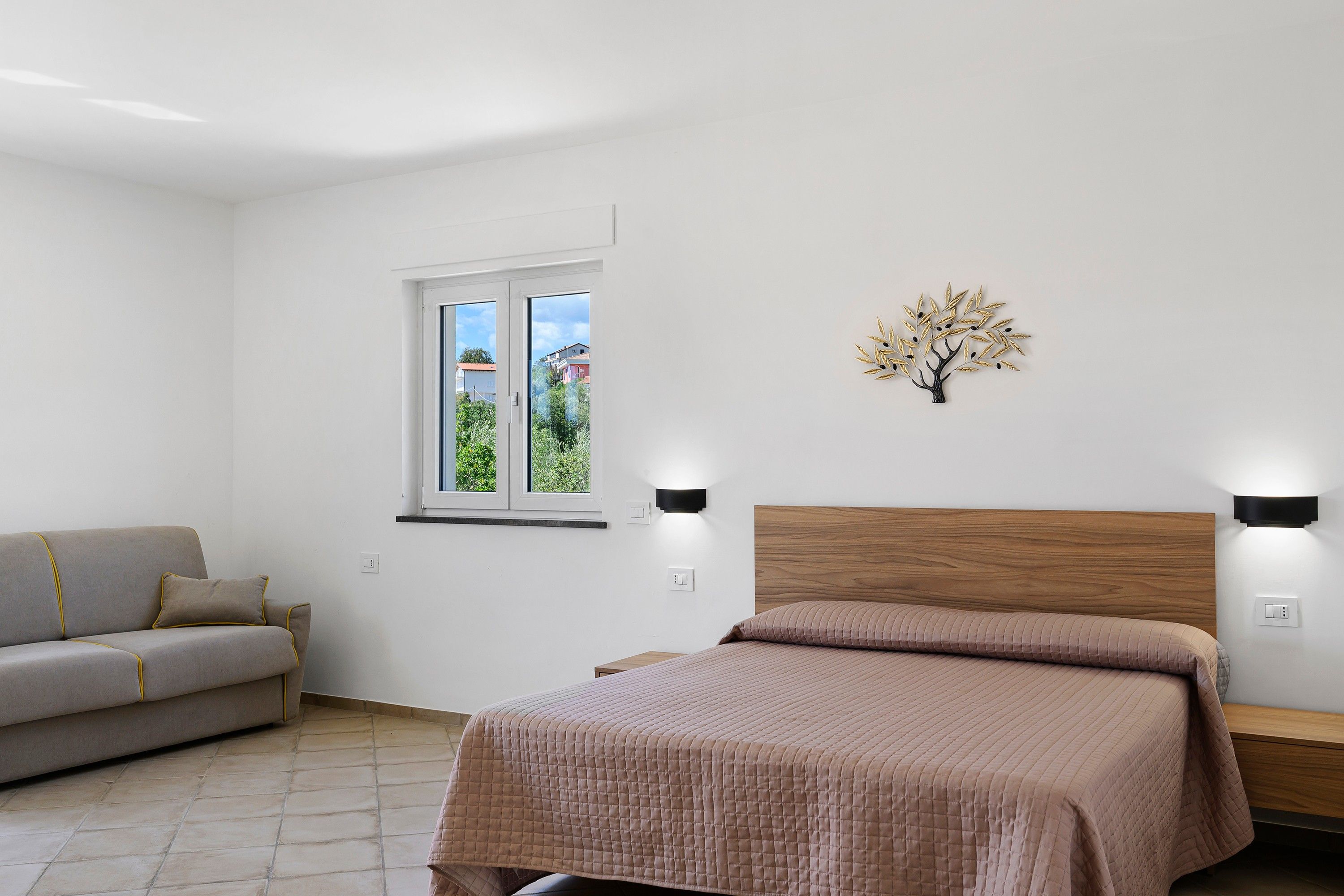 Ein Schlafzimmer mit einem Bett, einem Sofa, einem Fenster und einer Wandleuchte.