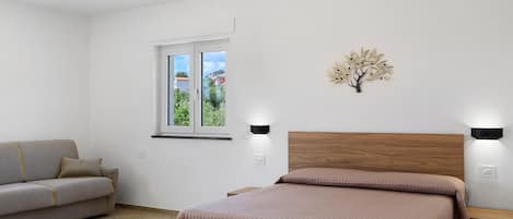 A bedroom with a bed, a sofa, a window, and a wall-mounted light fixture.
