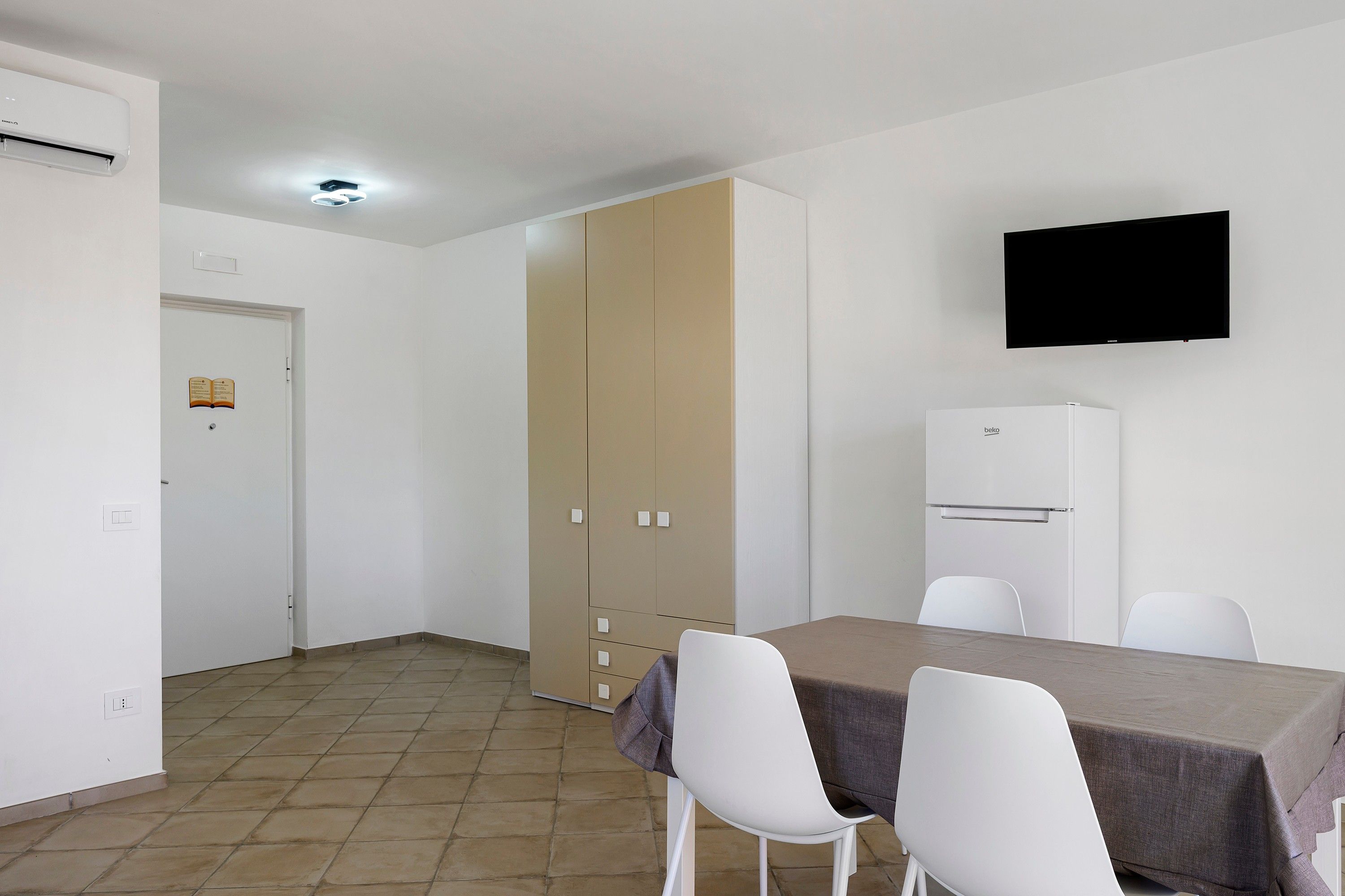 Una habitación pequeña y limpia con una mesa de comedor, sillas, televisor y refrigerador.