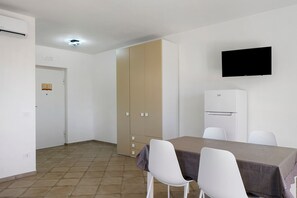 A small, clean room with a dining table, chairs, a TV, and a refrigerator.