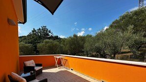 A rooftop terrace with a seating area, a table, and a view of trees and hills.