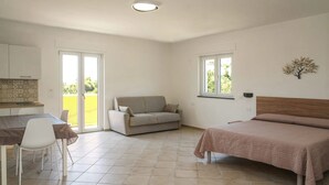 A bedroom with a bed, a sofa, a dining table with chairs, and a window.