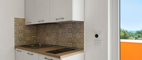 Una cocina con armarios blancos, un salpicadero estampado, un lavamanos de acero inoxidable y vistas al exterior.