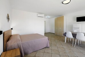A bedroom with a bed, a bedside table, a wardrobe, a desk with chairs, and a television mounted on the wall.