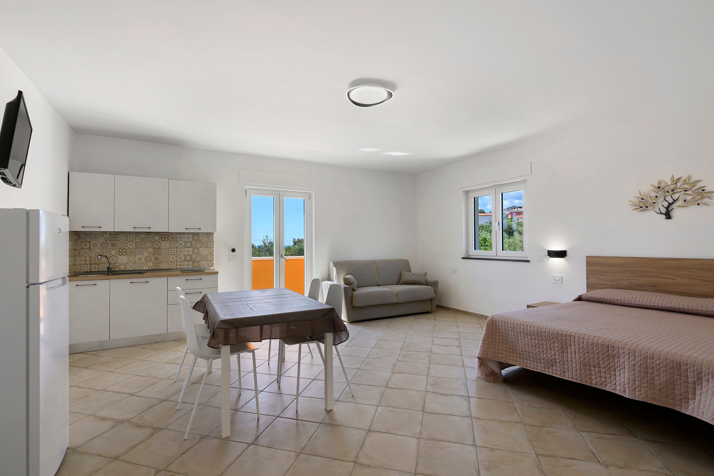 A compact living space with a kitchenette, a dining area, a sofa, and a bed.