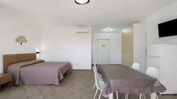 Una camera d'albergo con un letto, un comodino, una scrivania con sedie, una televisione e un frigorifero.