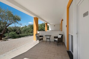 A covered outdoor area with two wicker chairs and a small table, a door with a sign, and a view of the surrounding landscape. - Oliblu Holiday Home - Standard Frantoio Studio (Vibonati)
