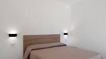 Un letto singolo con una testiera in legno in una stanza dalle pareti bianche e due luci a parete.