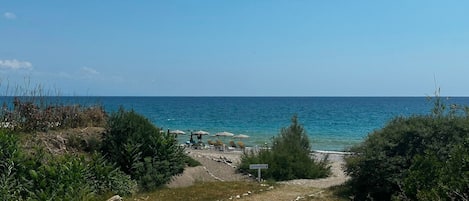 Un camino bordeando la playa, con sombrillas y sillas de descanso.