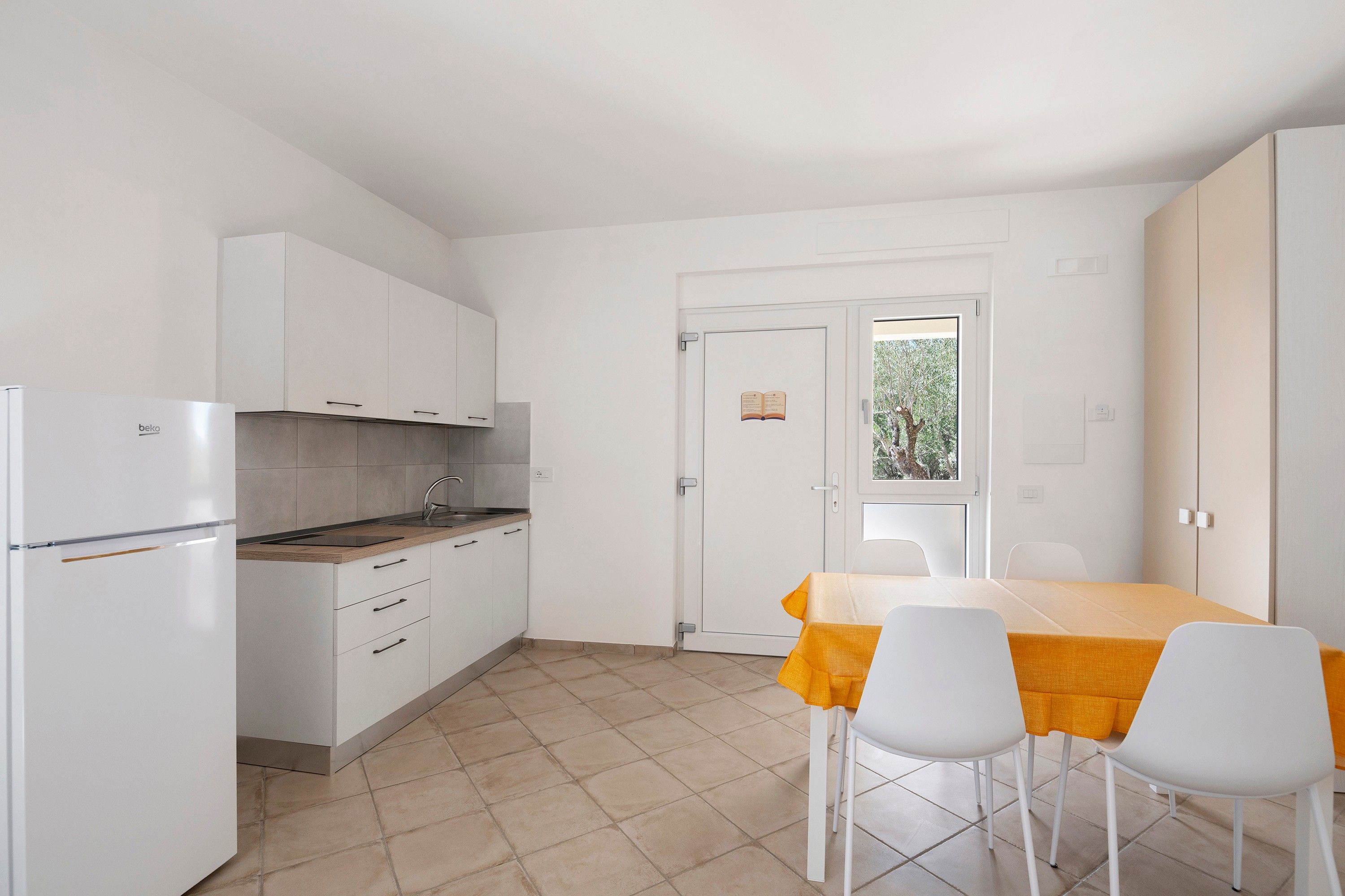 Une cuisine compacte avec des meubles blancs, un four encastré et un coin repas comprenant une table et des chaises.
