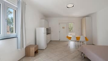 Une pièce de taille modeste comprenant un lit, une petite kitchenette, un coin repas avec une table et des chaises, et une porte donnant sur une autre pièce.