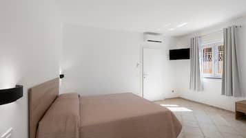 Une chambre d’hôtel avec un lit, un téléviseur fixé au mur, un appareil de climatisation, une porte et une fenêtre avec des rideaux.