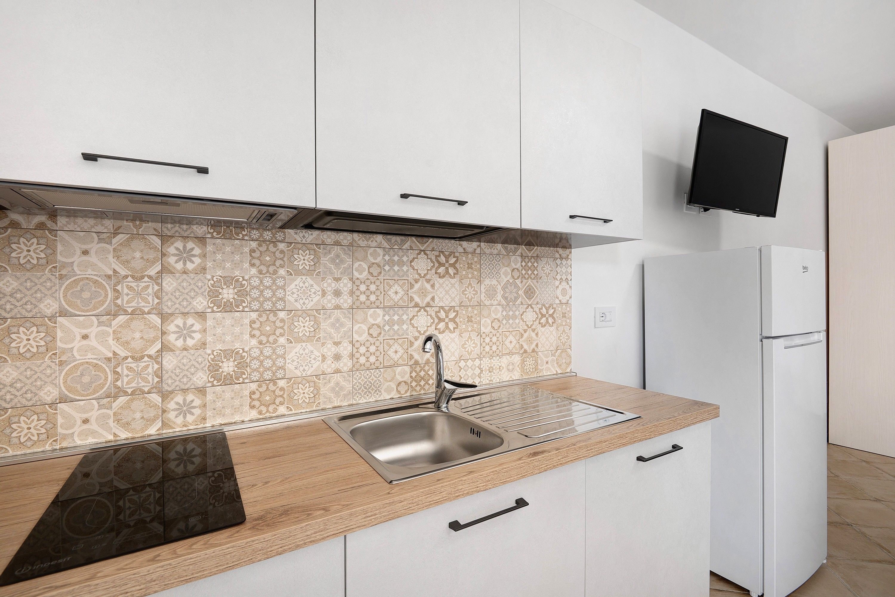 A modern kitchen with a patterned backsplash, stainless steel sink, wooden countertop, and a built-in oven.
