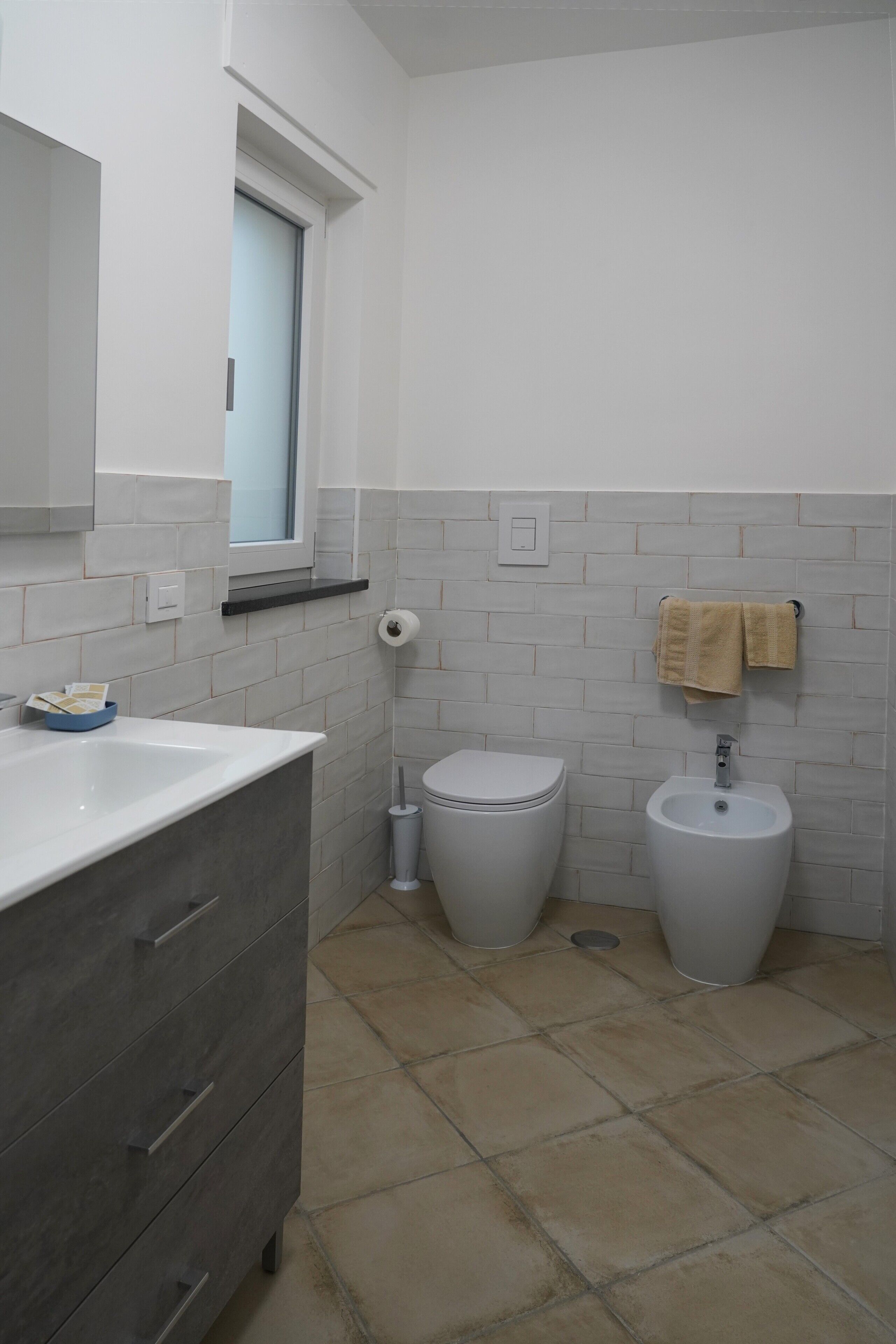 Een badkamer met een wit wastafelmeubel, een toilet, een bidet en een spiegel.