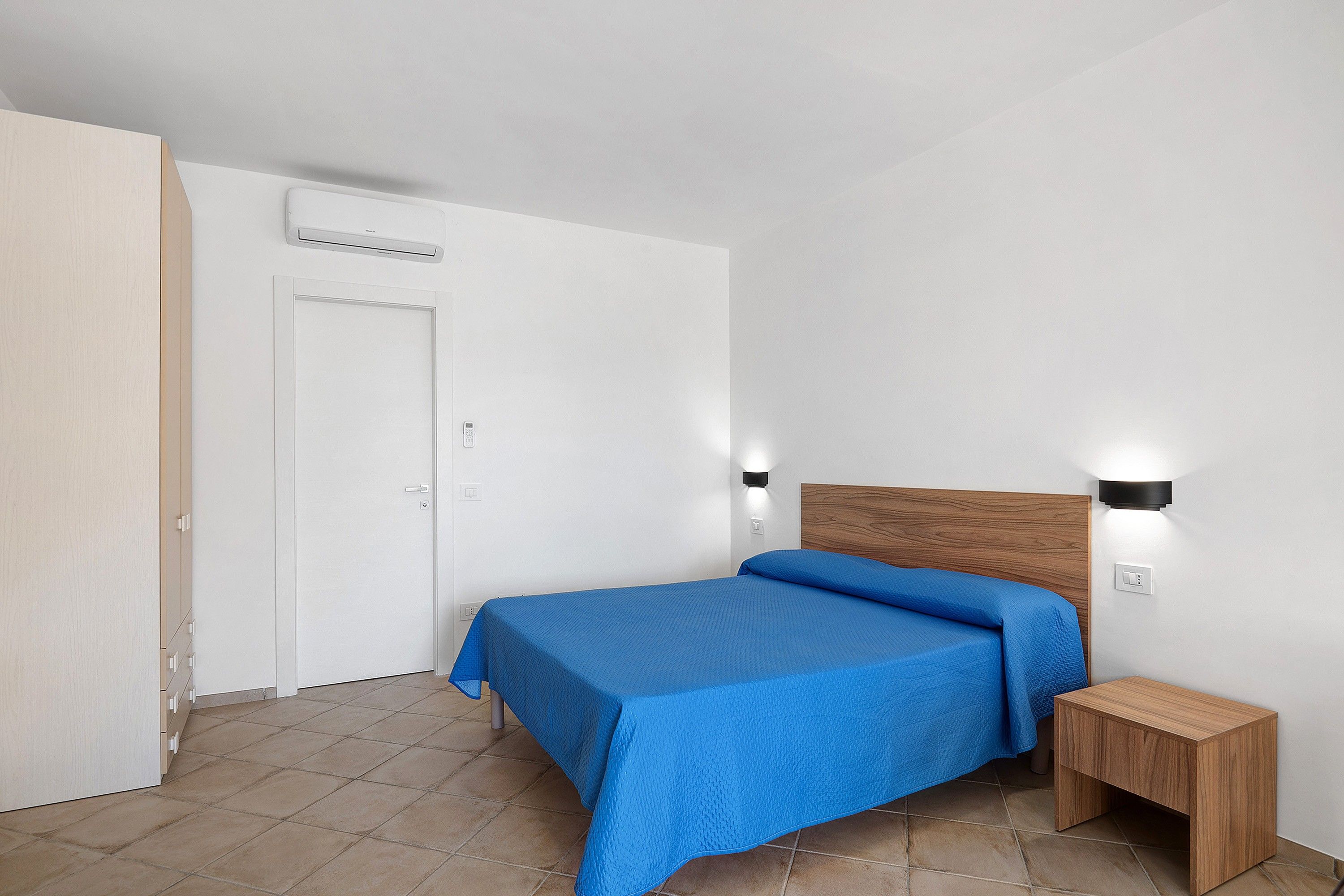 Une chambre à coucher comprenant un lit, une table de chevet, une lampe fixée au mur et un appareil de climatisation.