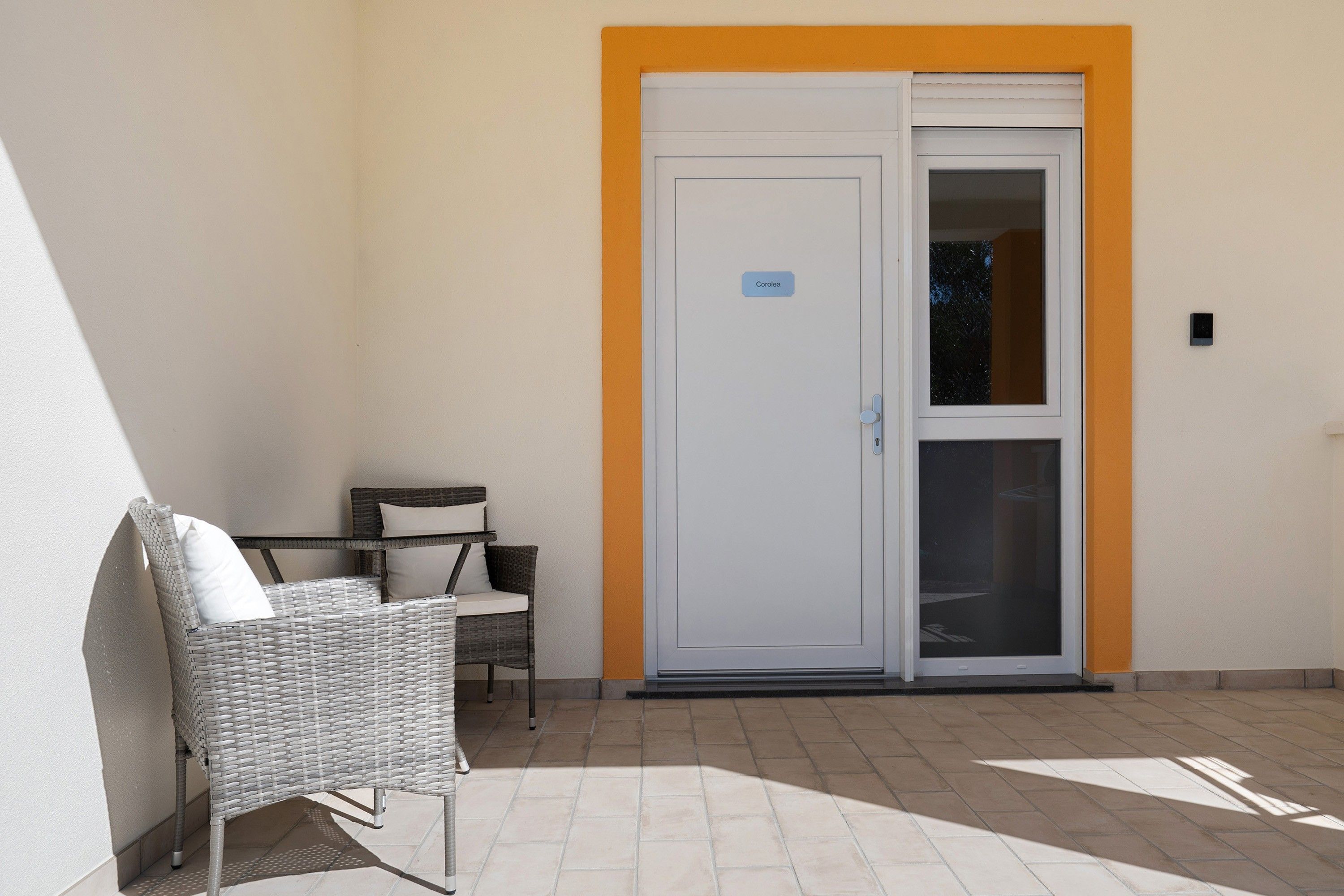 Une pièce avec une porte blanche, une petite table avec une chaise, et un fauteuil en osier.