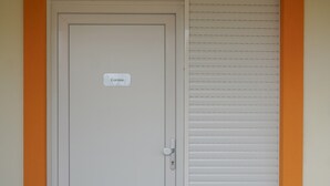 Eine Tür mit einem Schild, auf dem 'Corolea' steht, und eine Schiebetür mit horizontalen Rollläden.