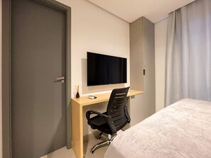 Ein Hotelzimmer mit einem Bett, einem Schreibtisch mit Stuhl, einem Fernseher und einer Tür.