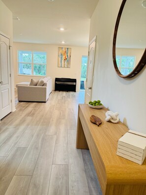 A modern interior with a wooden floor, a sofa, a bench, a mirror, and a bowl of apples. - Winter Haven 5BR Family Retreat- Near LEGOLAND + Disney, Family-Friendly (Winter Haven)