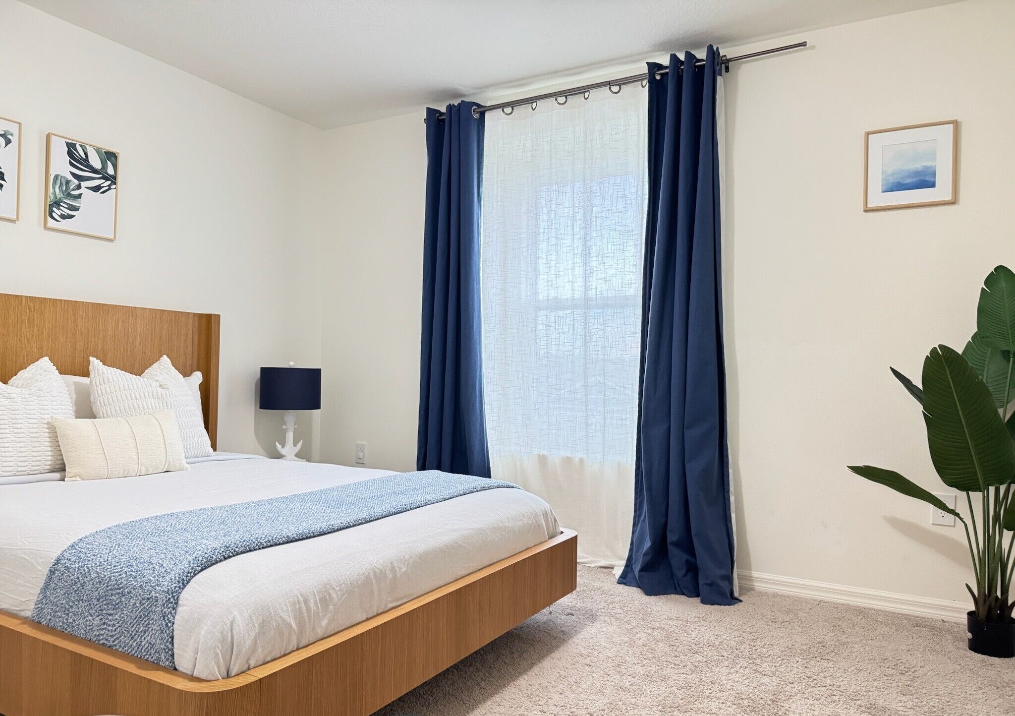 Une chambre à coucher avec un lit, des rideaux, une table de chevet, une lampe et une plante.
