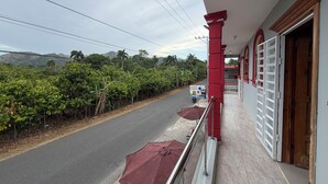 Ein Balkon mit Blick auf eine Straße und Grünflächen, eine rote Säule sowie ein Schild für ein Café.