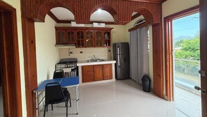 Eine Küche mit Holzschränken, einem Gasherd, einem Kühlschrank und einem Esstisch mit Stühlen.