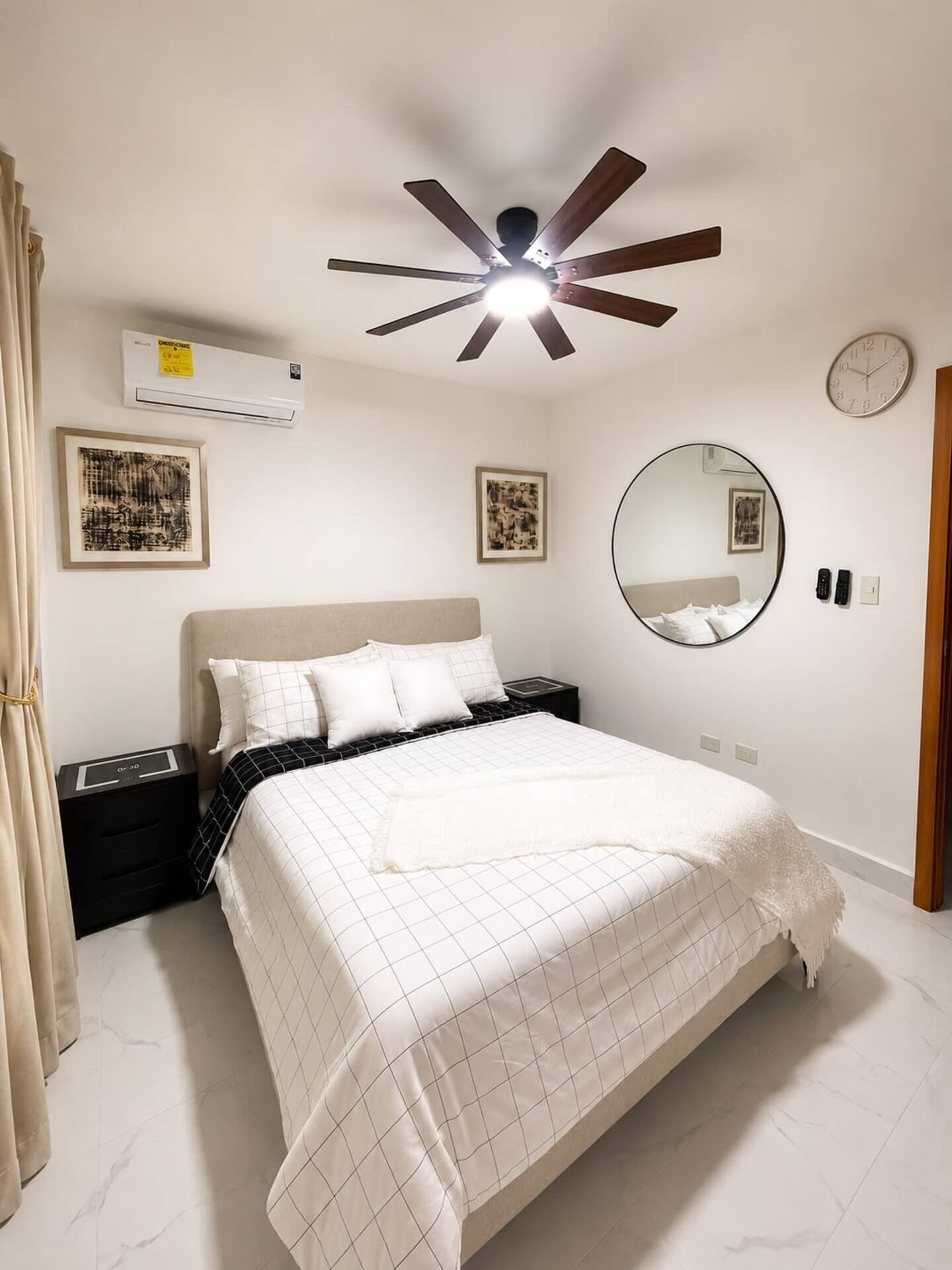 Un dormitorio con una cama, un ventilador de techo, un reloj de pared y cuadros enmarcados.