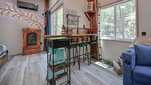 Tunnelmallinen olohuone, jossa on takka, baaritiski jakkaroineen, suuri ikkuna, josta avautuu näkymä puita kohti, ja sininen sohva.