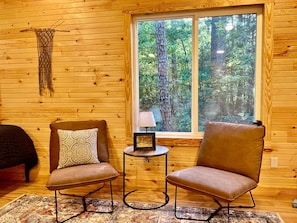 A cozy cabin interior with two leather chairs, a patterned rug, and a window offering a view of a forest. - The Quiet Pine Tiny Cabin (Scott County)