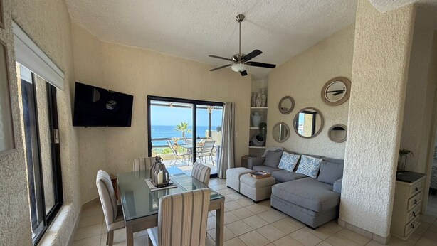 A living room with a glass dining table, sofa, and a ceiling fan. - Peaceful 2BR/2BA condo with Wrap-Around patio that overlooks the Sea of Cortez. (Cabo San Lucas)