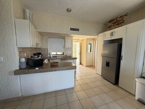 A kitchen with white cabinets, a granite countertop, a stainless steel refrigerator, and a window with a view. - Peaceful 2BR/2BA condo with Wrap-Around patio that overlooks the Sea of Cortez. (Cabo San Lucas)