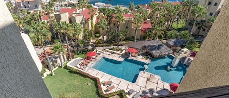 A resort with a swimming pool, palm trees, and a view of the ocean.