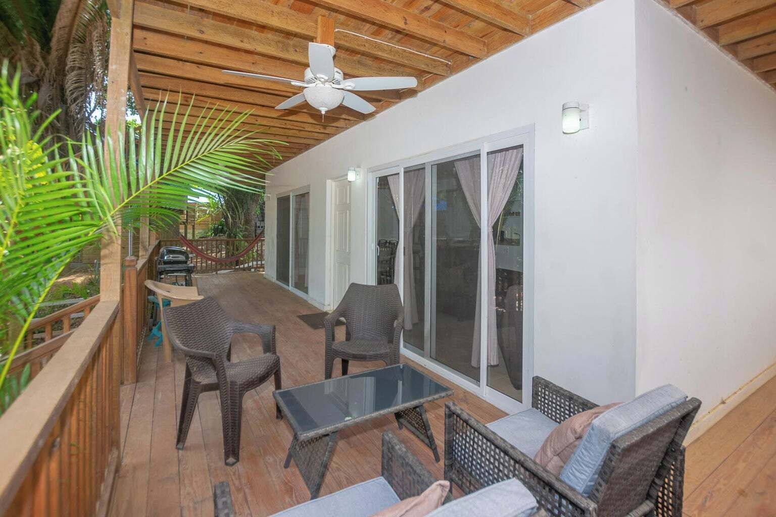 A covered outdoor seating area with wicker furniture, a ceiling fan, and large sliding glass doors.