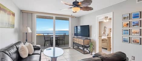 Een moderne woonkamer met een leren bank, een flatscreen televisie, een eethoek met stoelen en een balkon met uitzicht op zee.