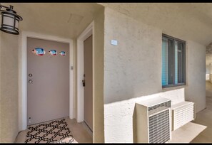 A hallway with a door, a wall-mounted light fixture, and a window with blinds. - Beautiful 2/2 on the Gulf... see Sunsets and Dolphins from balcony (Hudson)