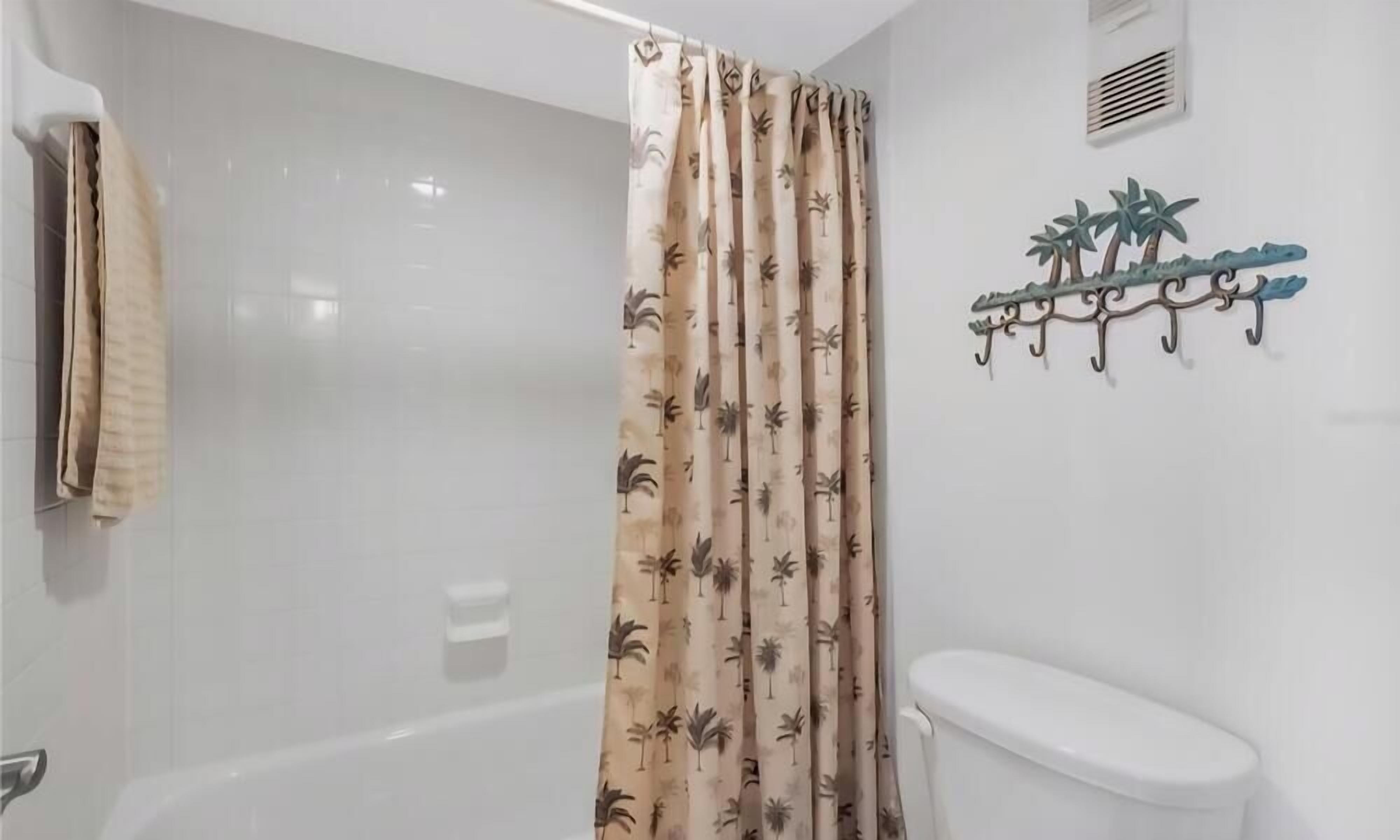 Un baño con bañera, inodoro y cortina de ducha con estampado de palmeras.