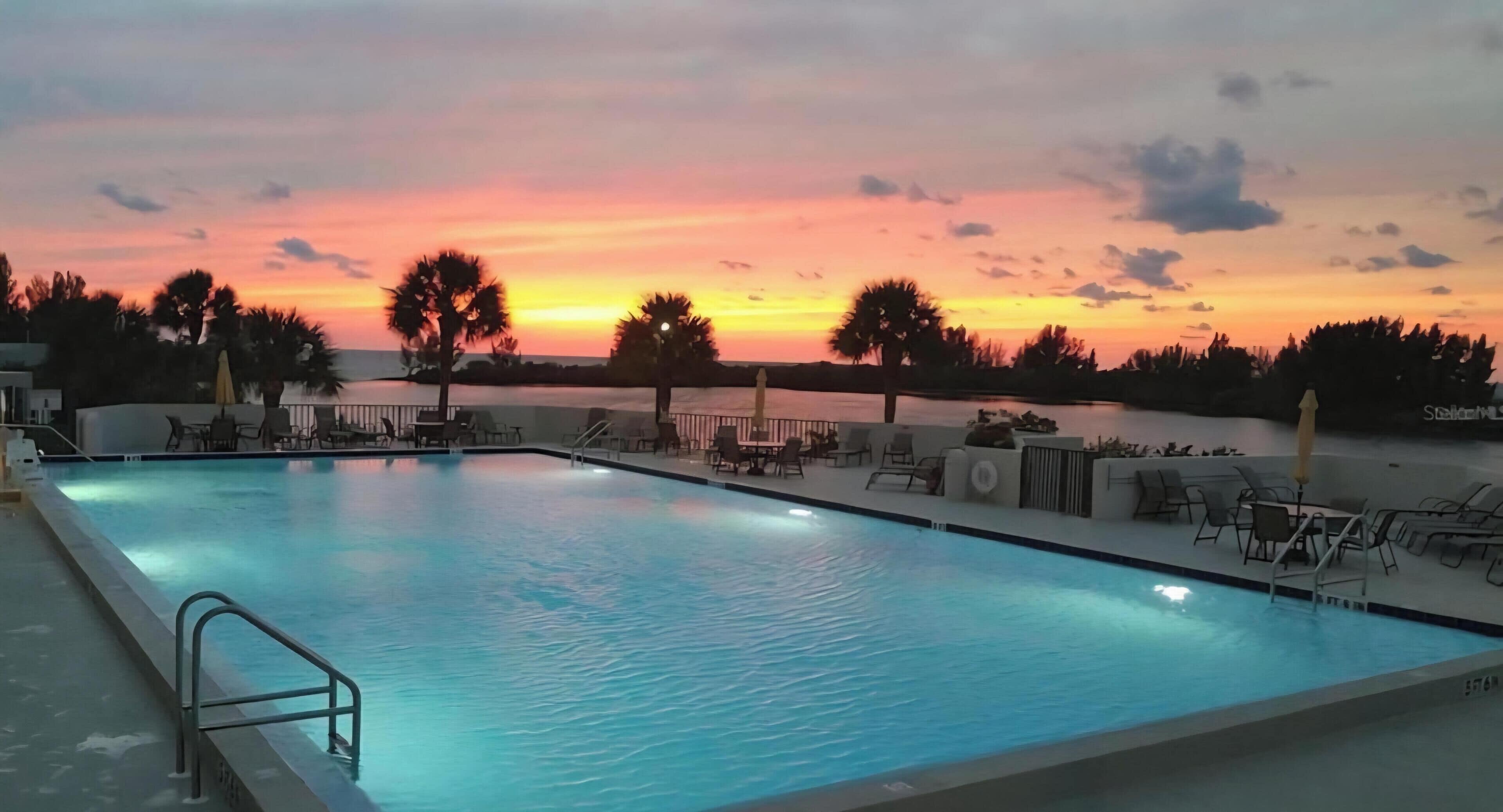 Une piscine entourée d’arbres, avec des chaises longues et des parasols, offrant une vue imprenable sur le coucher de soleil.
