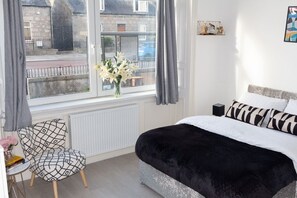 A bedroom with a bed, a chair, a window with curtains, and a radiator.