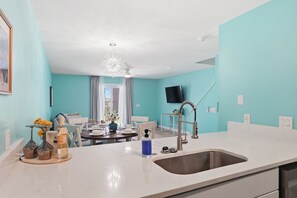 A modern kitchen with a large sink, a dining area with a table and chairs, and a television mounted on the wall. - Sapphire Shores, Steps to the Beach, Sleeps 8 (Panama City Beach)