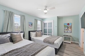 Ein Schlafzimmer mit zwei Betten, einem Deckenventilator, einer Tür mit satinierten Glasscheiben und Bildern an den Wänden.