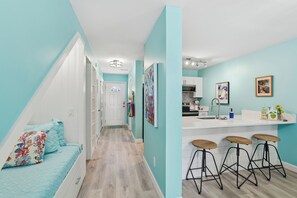 Una cocina moderna con taburetes de bar, encimera blanca y vista al dormitorio contiguo.