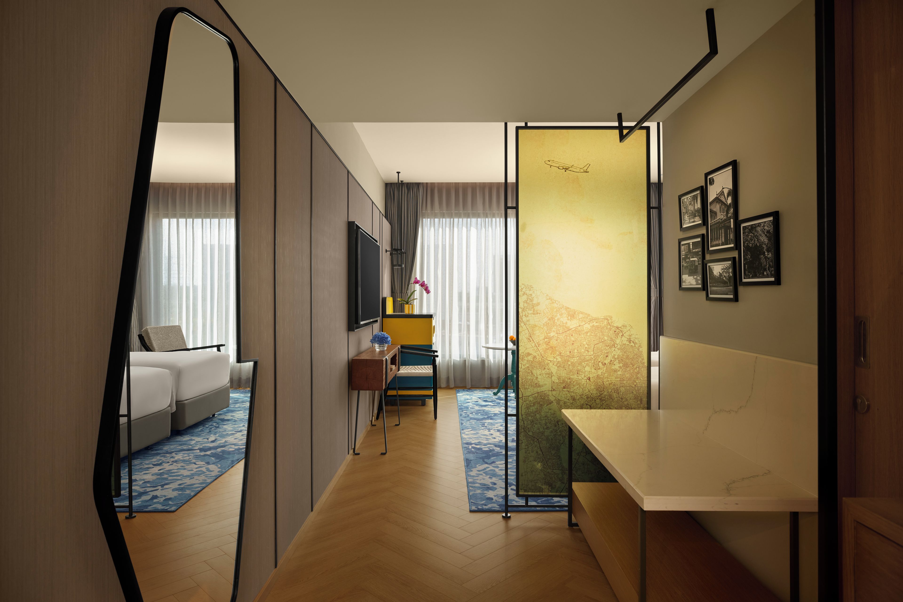 Une chambre d’hôtel avec un grand miroir, un canapé, une petite table sur laquelle est posé un vase de fleurs, et une carte accrochée au mur.
